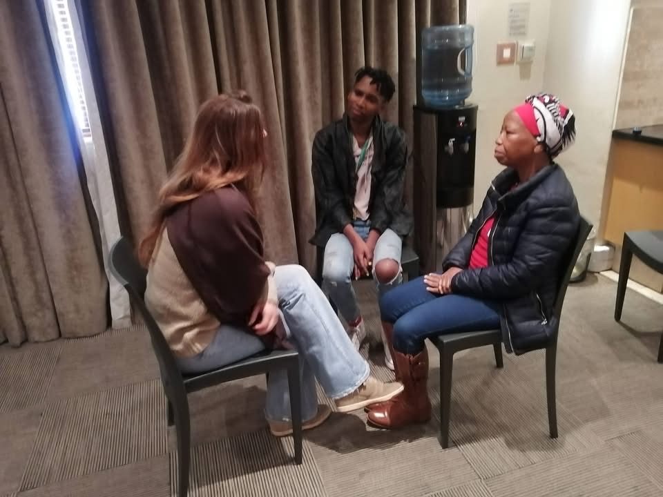 Three participants seated on chairs facing each other, sharing and listening