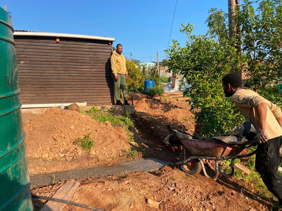 People working with a wheelbarrow beside the wooden centre building